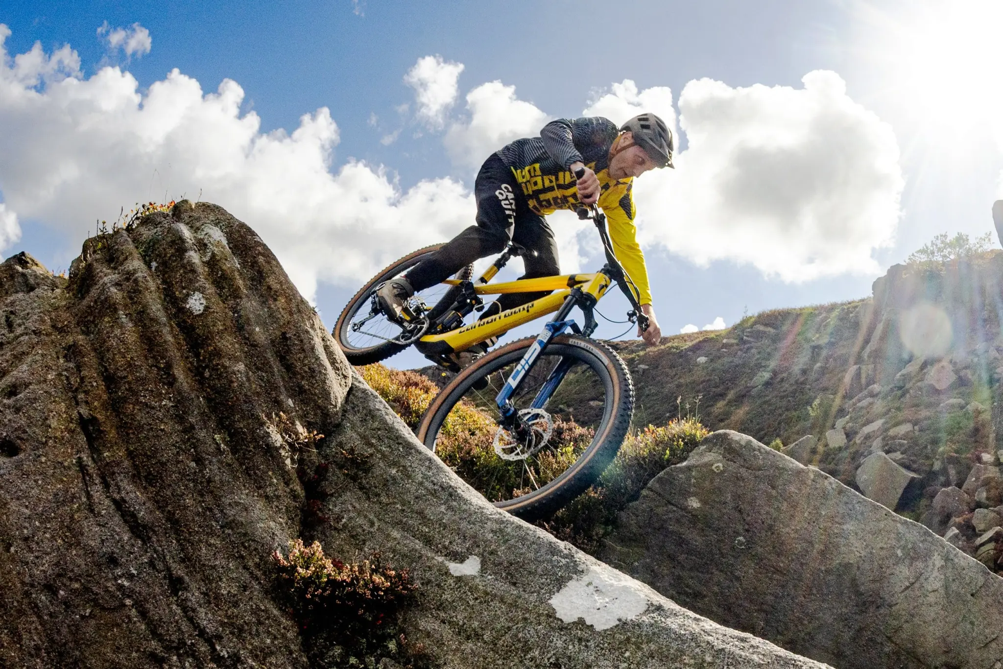 A rider in a yellow jersey descends rocks on a yellow Carbon Wasp mountain bike