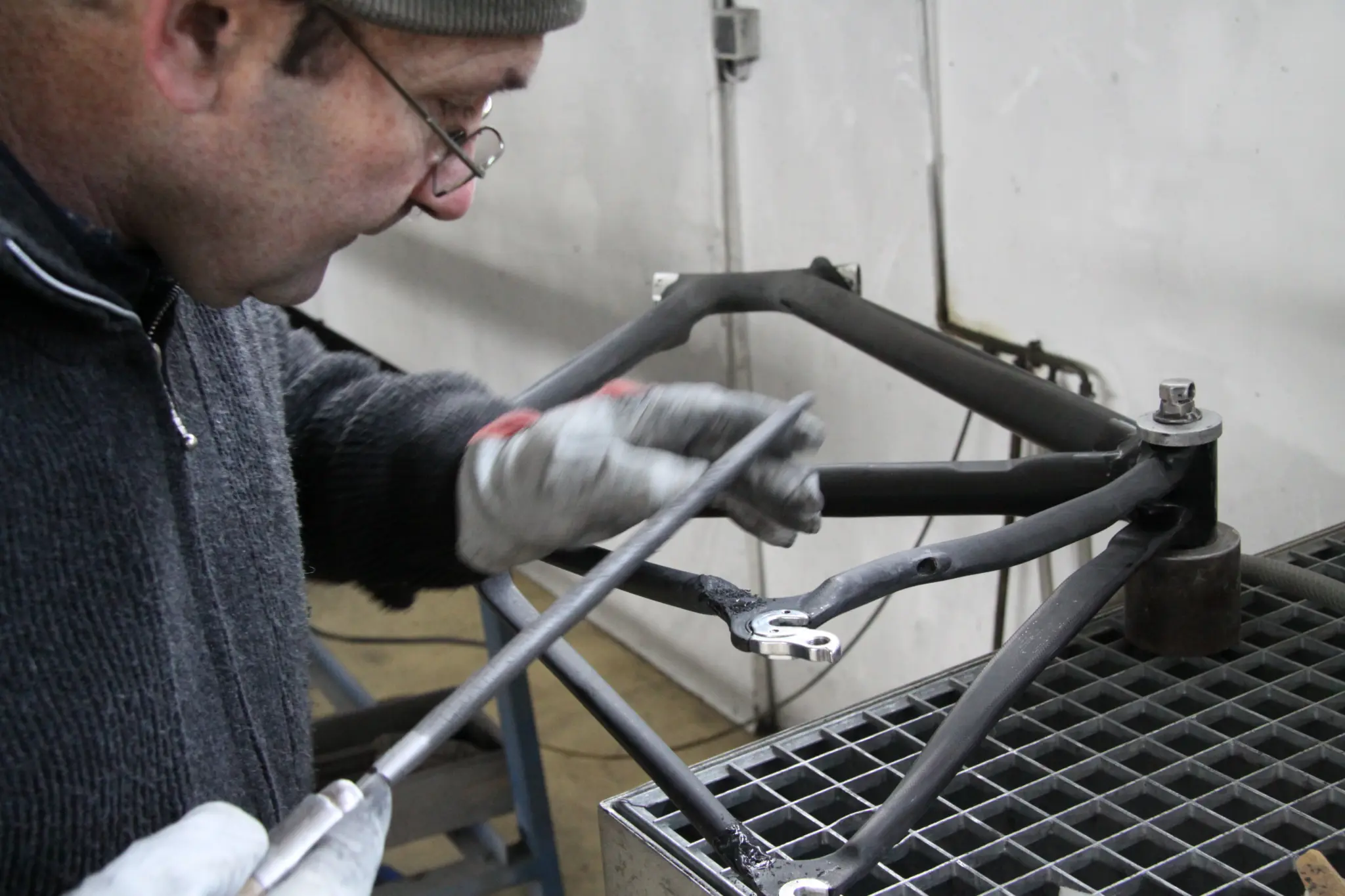 A craftsman works on the rear triangle of a bicycle frame on a workbench